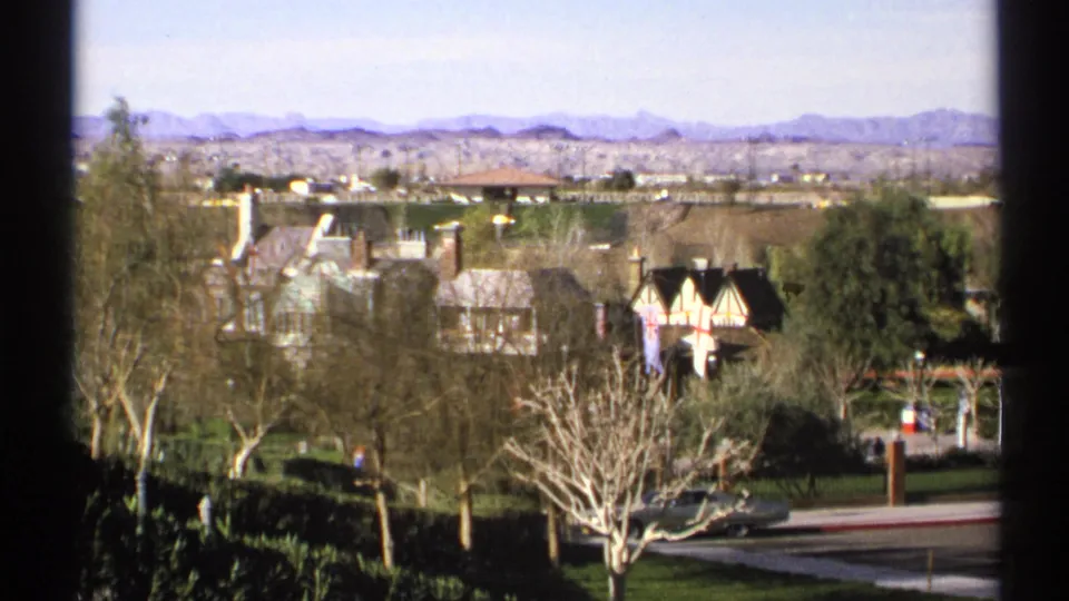 1972 Arizona 8mm frame showing Tudor-style buildings, landscaped grounds, bare trees, roadway, and a mountain horizon.