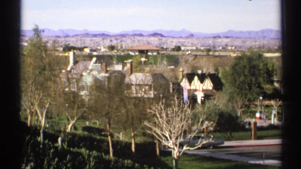 1972 Arizona 8mm frame holding on the English Village setting, with Tudor-style roofs, lawns, trees, road, and distant mountains.