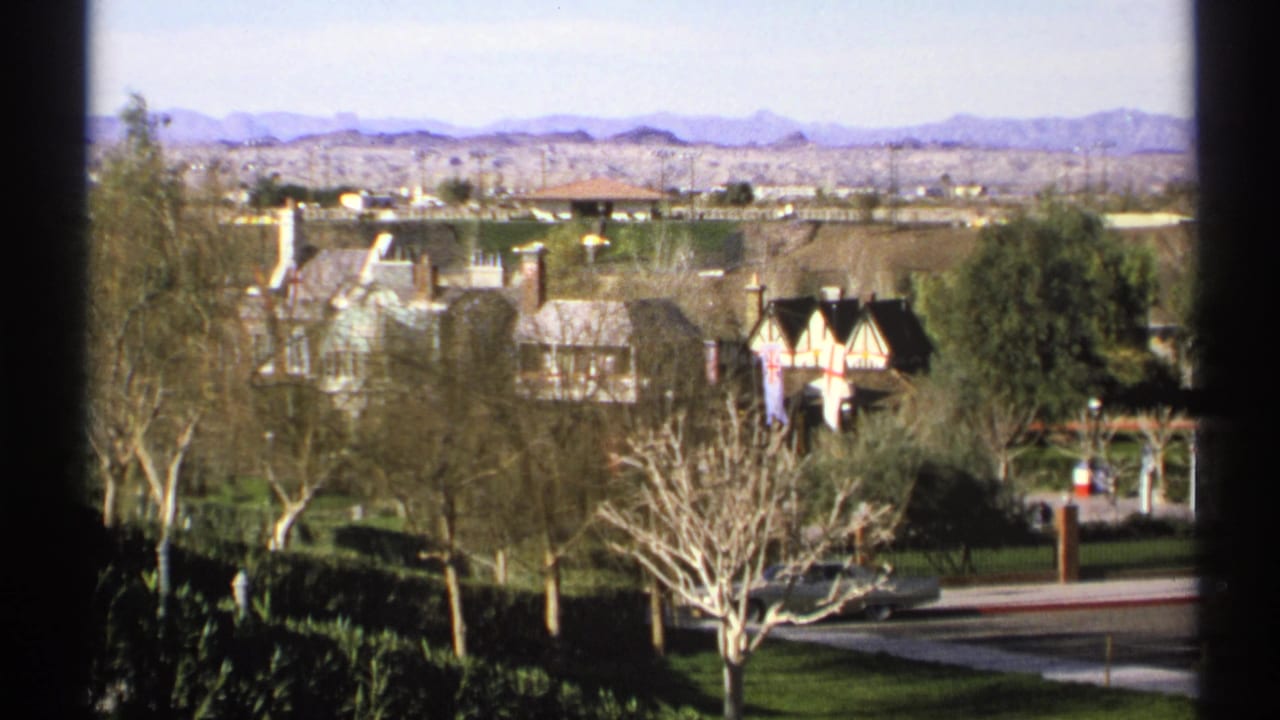 Elevated view of suburban houses, trees, mountains, water, and flagpoles in bright daylight.