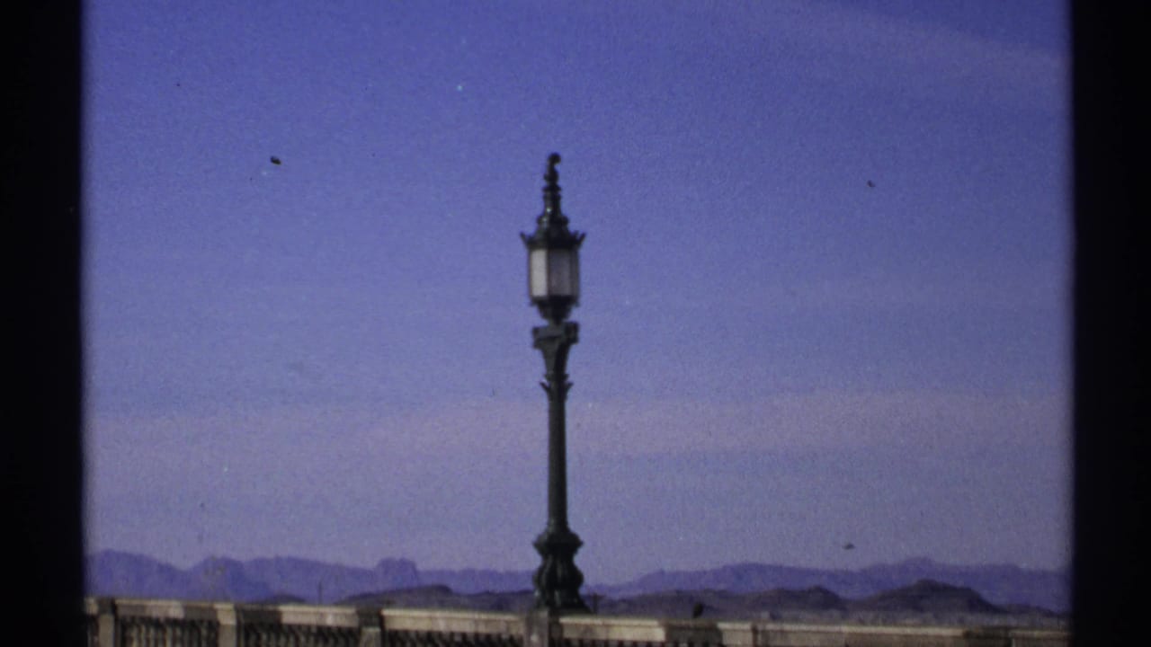 Ornate street lamp above a stone railing with blue sky and distant desert mountains.