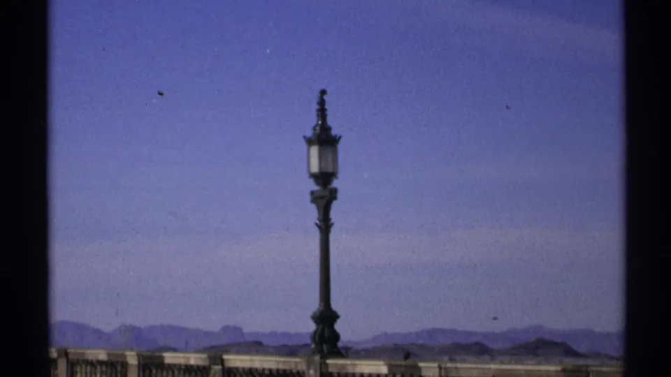 1972 Arizona 8mm frame showing an ornate street lamp on a stone balustrade against a blue sky and low desert mountains.