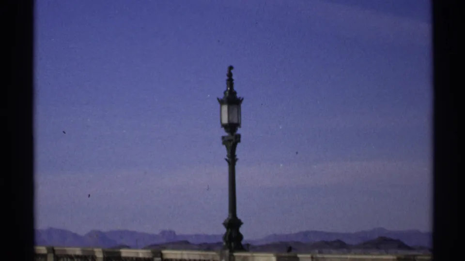 1972 home-movie view of a tall decorative lamp and stone railing, with hazy Arizona mountains under a blue sky.