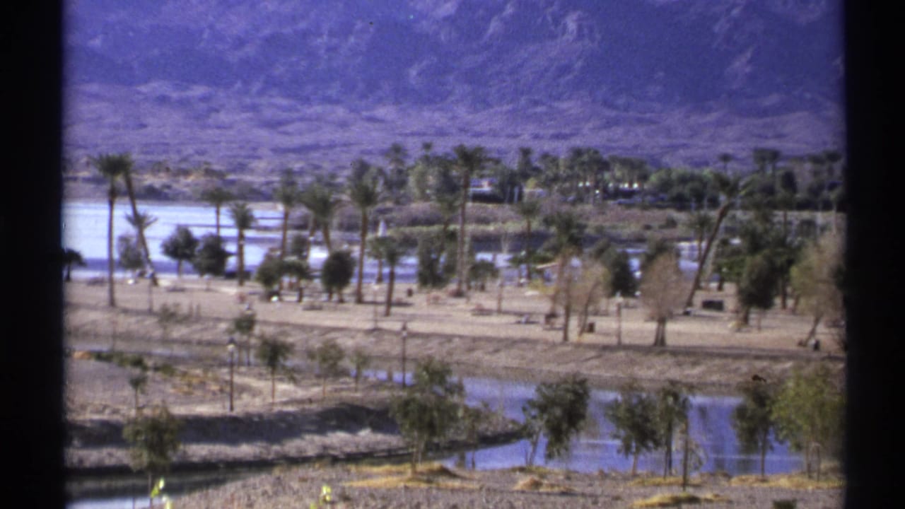 1972 Arizona home-movie view of palms, dry ground, water, and distant mountains, framed by dark window-like edges.