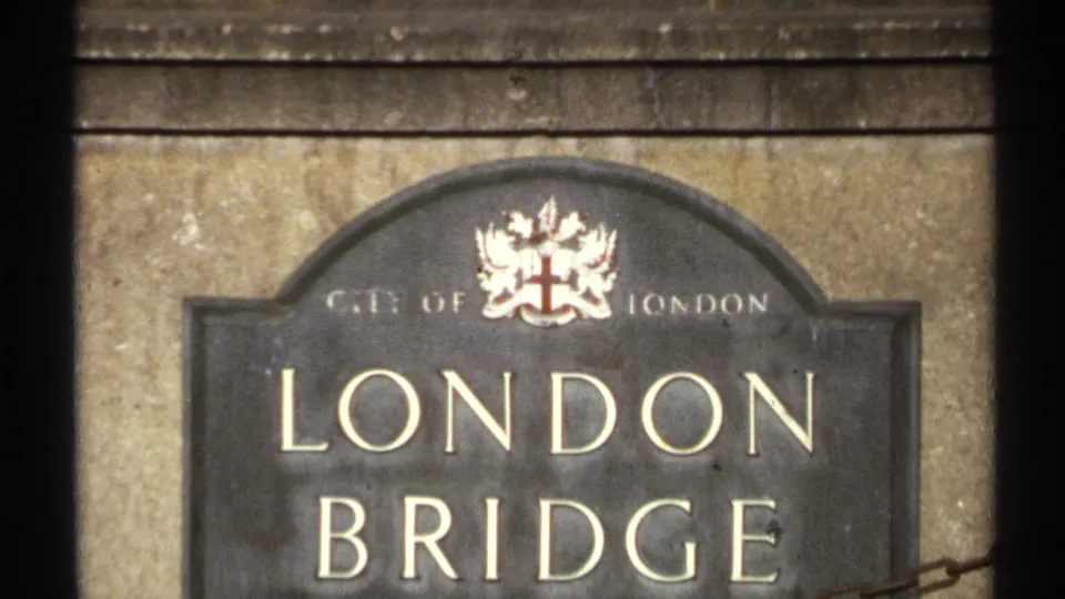 Close view of a London Bridge sign beneath the scenic Arizona waterway and palm landscape, with a civic-style crest visible.