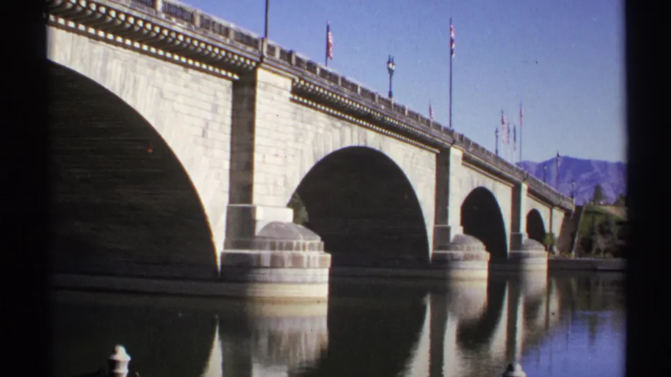 1972 Arizona 8mm frame with a closer look at the stone bridge arches, water reflections, flagpoles, and mountain backdrop.