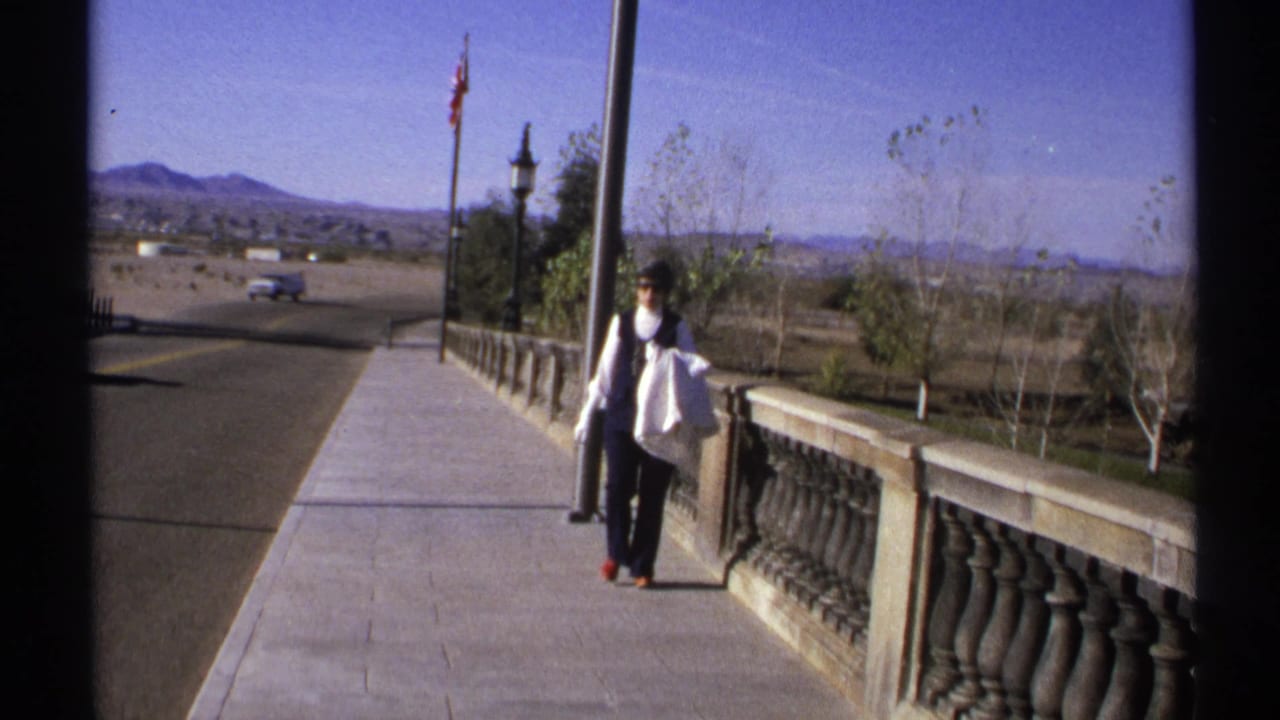 Woman walking along a stone balustrade beside a road with mountains in the distance.