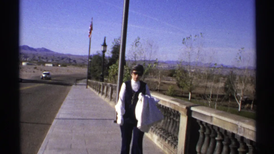 Near the end of the clip, the woman passes close to camera on the 1972 Arizona walkway, with road traffic and mountains behind her.
