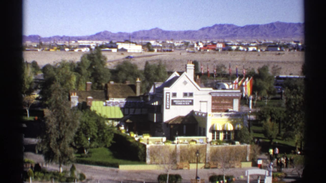1972 Arizona home-movie frame of the Bridgewater Terraces building, landscaped trees, flags, desert flats, and distant mountain range.