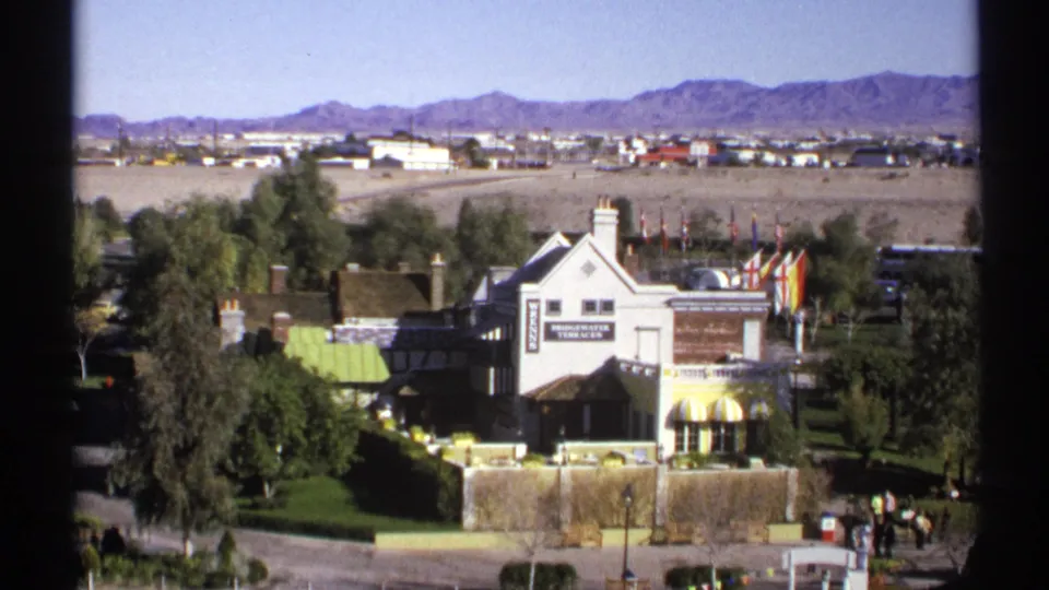 1972 Arizona frame showing Bridgewater Terraces from above, with flags, landscaped grounds, desert background, and small figures near the entrance.