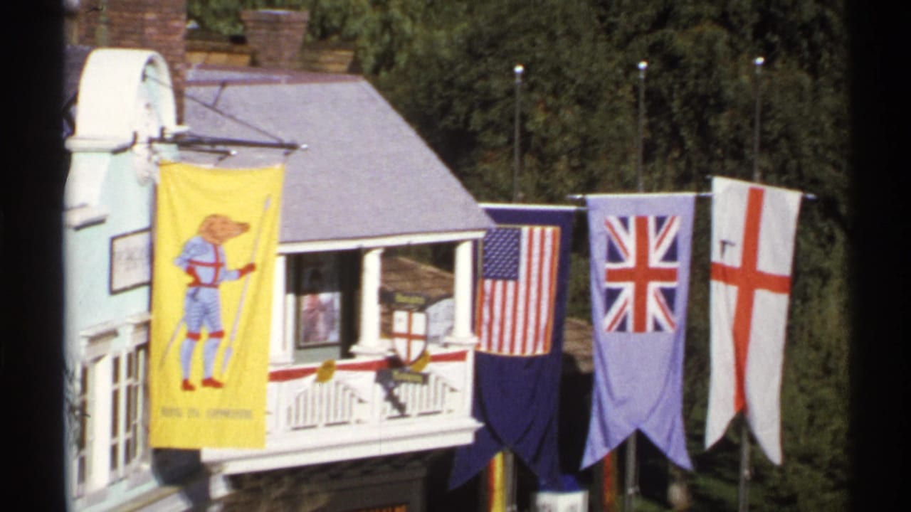 1972 Arizona 8mm frame showing a miniature village facade with a yellow cartoon dog banner, U.S. flag, Union Jack, and St. George's Cross banner.