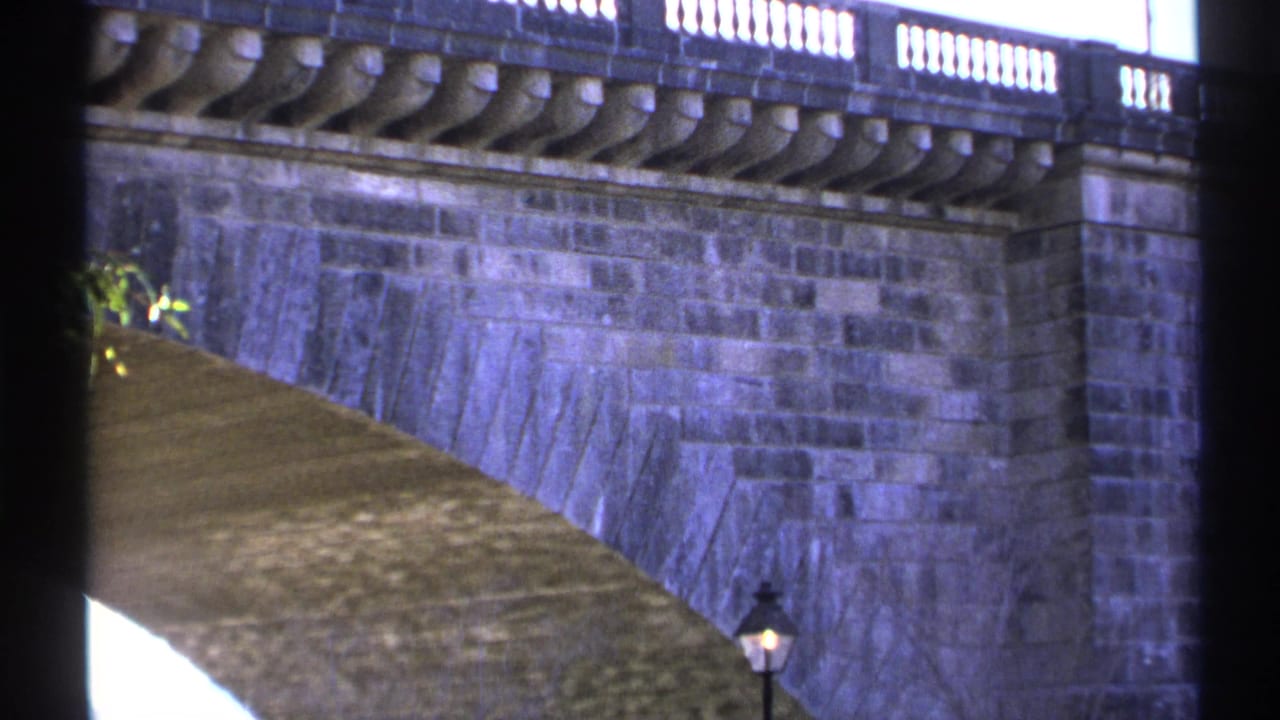 Stone arch bridge with balustrade, lamppost, and dark vertical film-edge bars.