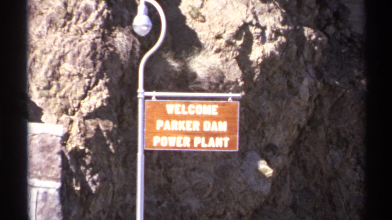 Welcome sign for Parker Dam Power Plant mounted beside a rocky canyon wall.