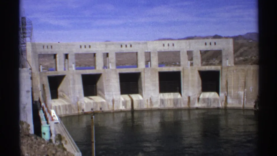 Wide 1972 Arizona 8mm frame of Parker Dam Power Plant, showing its concrete face, spillway openings, and calm water.