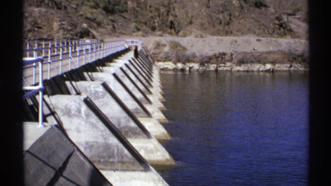 Concrete bridge or dam edge with metal railings crossing calm river water.