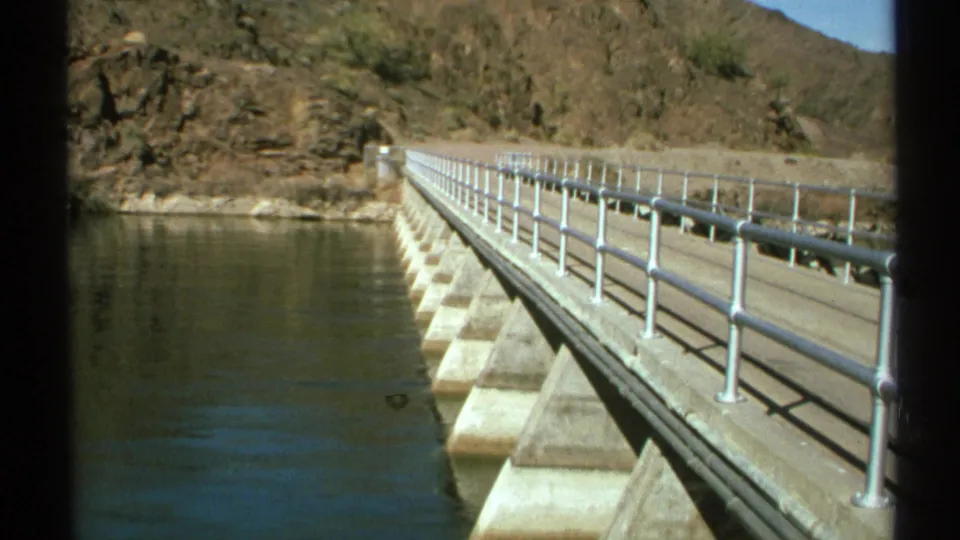 A second 1972 Arizona view of the bridge or dam walkway, with railings, concrete supports, water, and desert rock in bright sunlight.