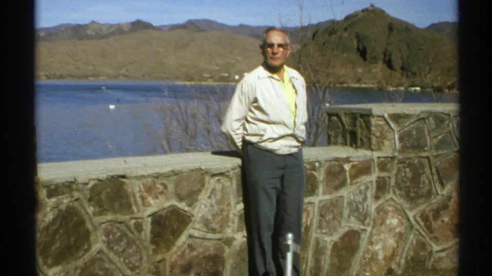 A 1972 Arizona visitor portrait shows an adult man at a stone overlook, facing the camera with lake water and rugged hills behind him.