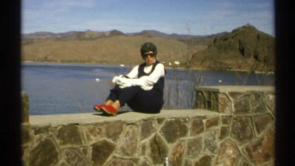A closer 8mm frame shows the woman sitting on the wall, wearing sunglasses and red shoes, with the Arizona lake and hills behind her.