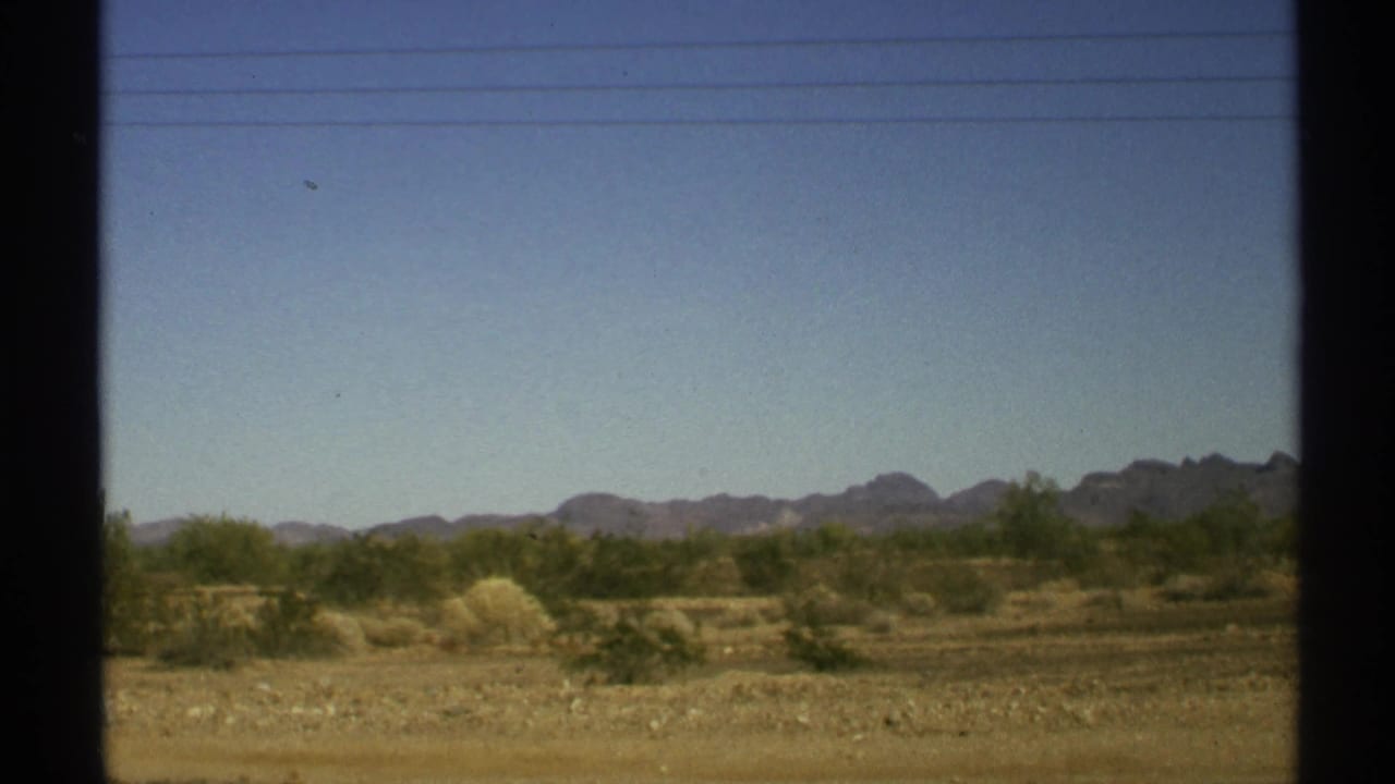 Desert shrubs and distant mountains seen through dark vehicle window trim.