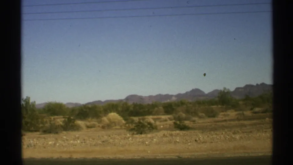 1972 Arizona roadside desert with brush, sandy terrain, power lines, and mountain silhouettes seen through dark window trim.