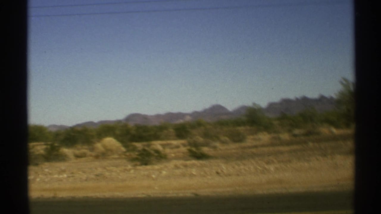 Blurred desert landscape seen through dark vehicle-window edges.