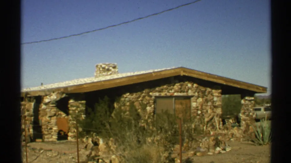 1972 Arizona 8mm frame with a closer view of the stone house exterior, chimney, dry yard, shrubs, and overhead wire.