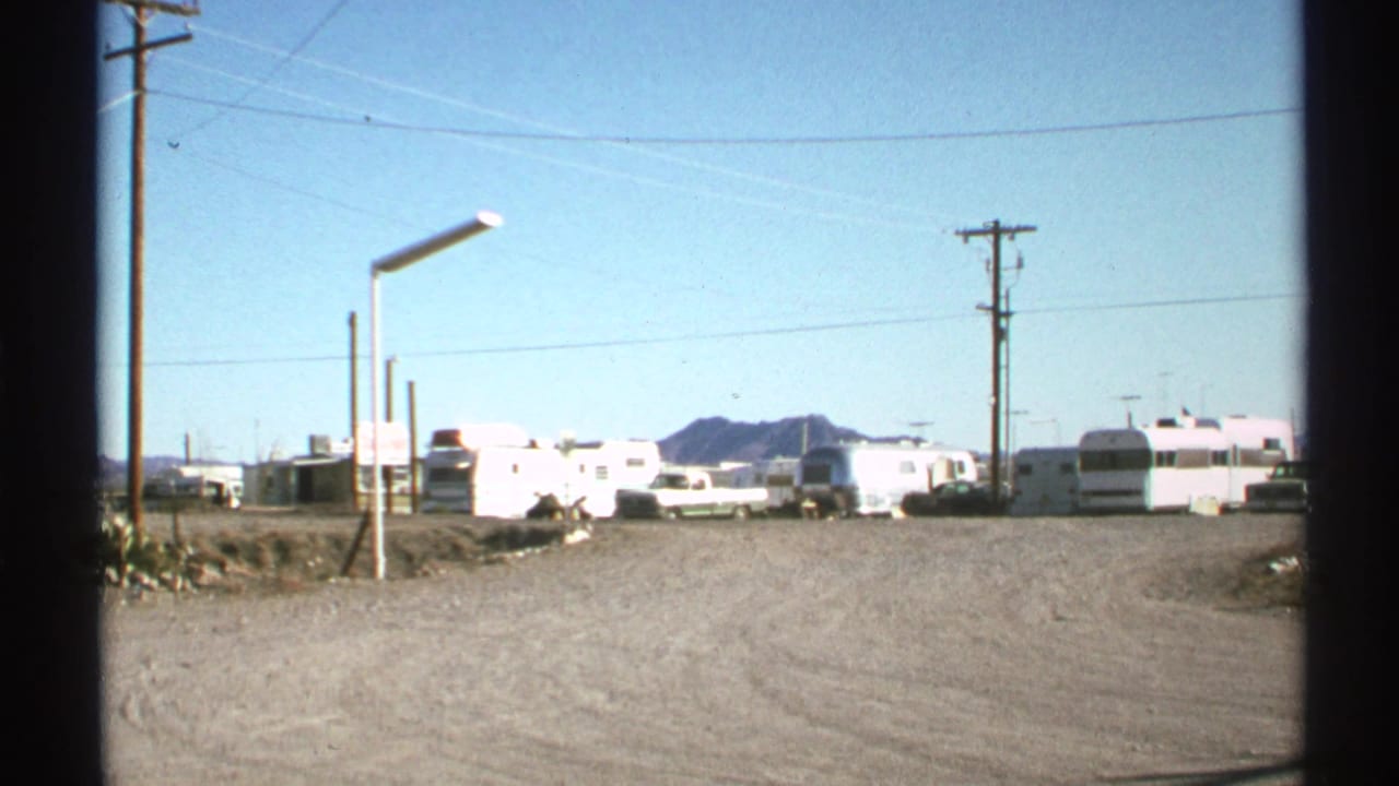 Dusty campground road with trailers, utility poles, wires, and mountains beyond.