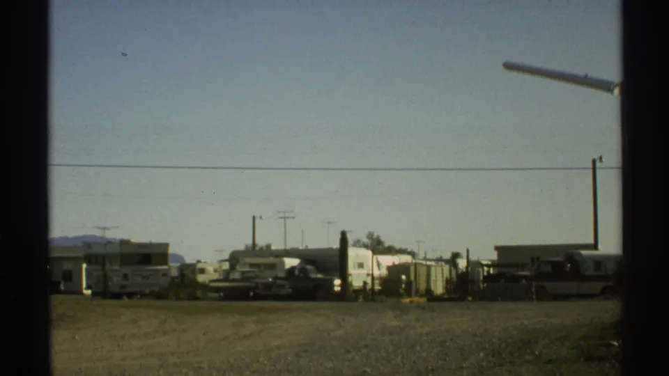 The Arizona roadside lot remains in view, showing parked trailers, RVs, utility lines, a streetlamp, and mountains in the distance.