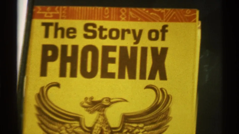 Close handheld 8mm view of the yellow The Story of PHOENIX cover, with the title and phoenix graphic filling the frame.