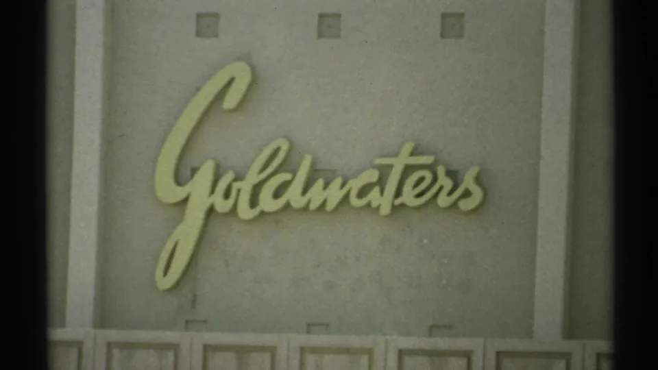 1972 Arizona 8mm frame showing a raised cursive Goldwaters sign on a pale gray paneled wall, with film edges visible.