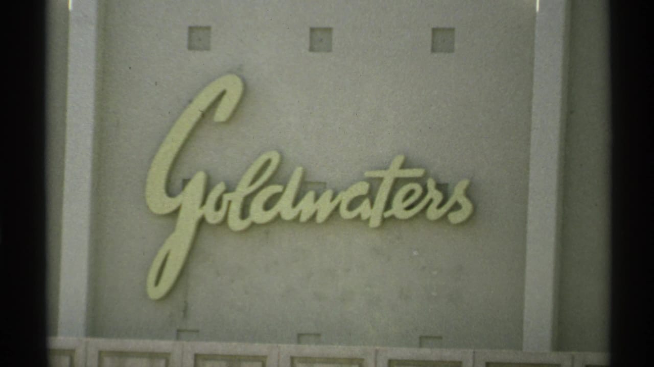 Close view of Goldwaters cursive sign mounted on a plain exterior wall.