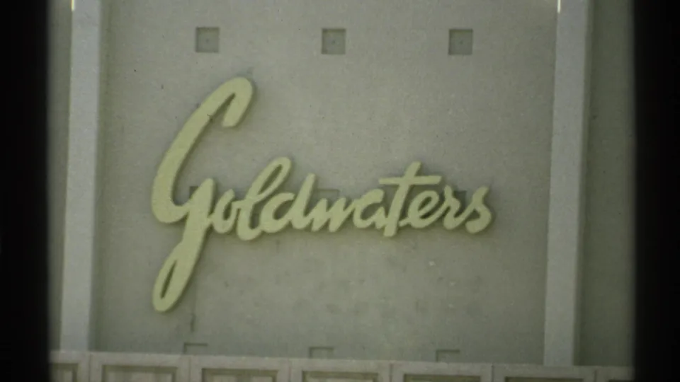 1972 Arizona 8mm frame showing the Goldwaters department-store sign in cursive lettering on a light exterior wall.