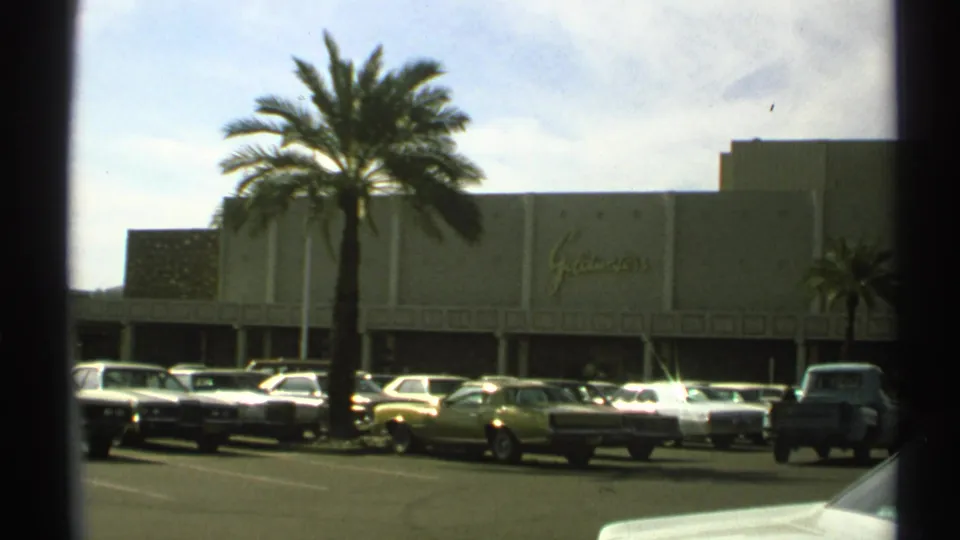 1972 Arizona 8mm frame showing the Goldwaters exterior partly framed by a tall palm and parked cars.