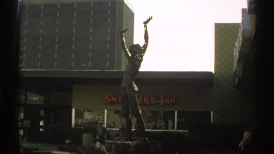 1972 Arizona 8mm frame showing a tall statue outside a building marked Smoker's Inn, with pedestrians near the entrance.