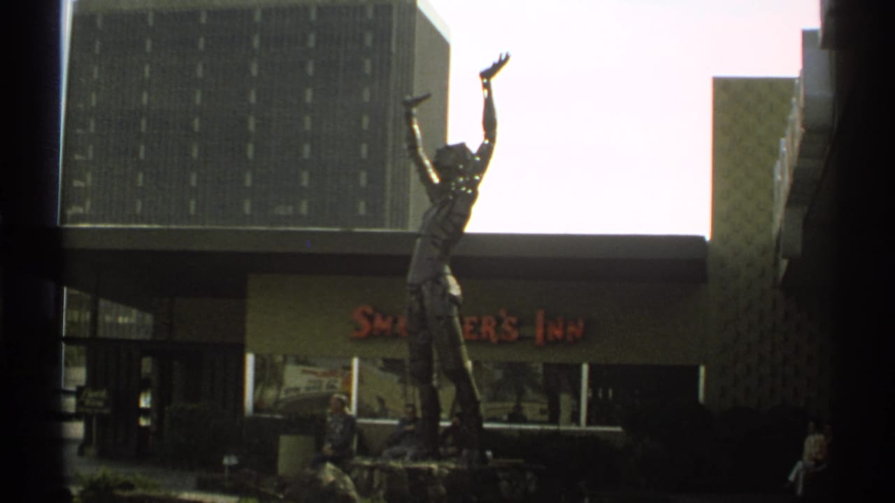 Raised-arm statue outside Smokey's Inn with a tall building behind it.