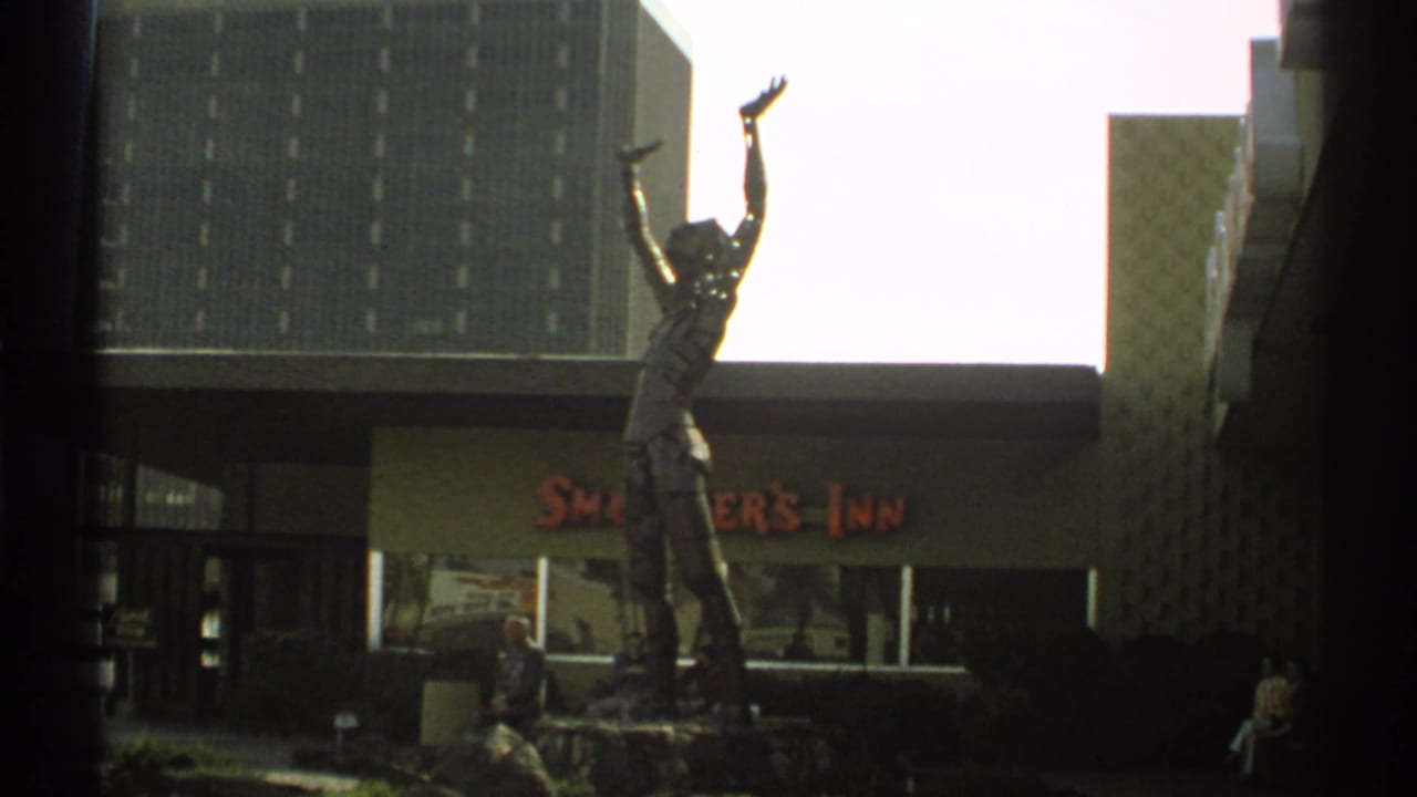 Statue outside Smokey's Inn beside a modern building and seated visitors.