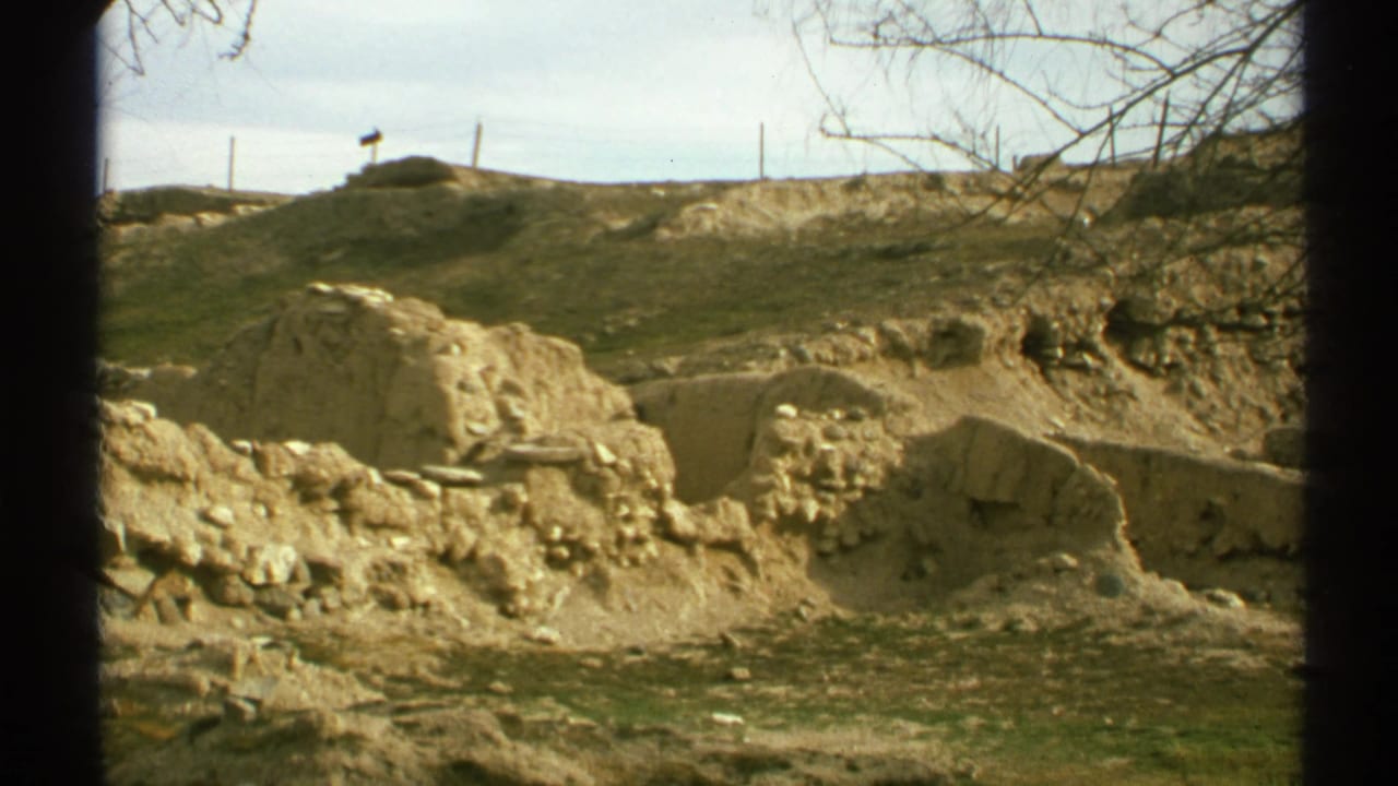 Exposed earth and eroded soil walls under a bright sky with dark film-frame borders.