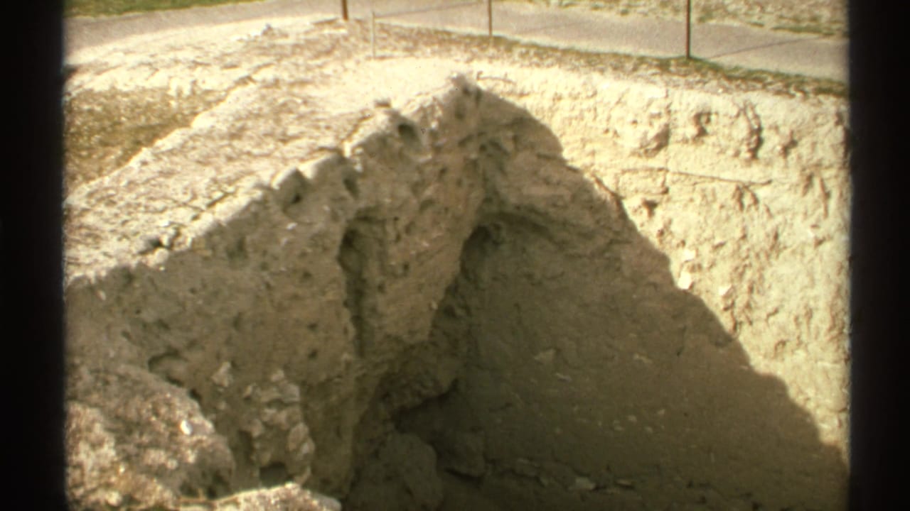 Close view of tan excavated trench walls beside a paved edge in bright sun.
