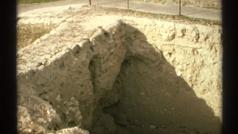 1972 Arizona 8mm frame showing sunlit tan excavation walls and rough earthen edges near a paved walkway.