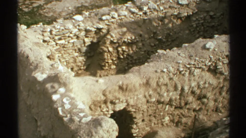 1972 Arizona 8mm frame with a closer view of sunlit ruin walls, pale soil, and dark vertical foreground bars.