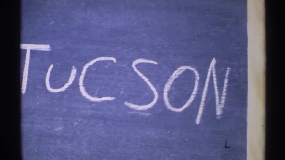 Blue handwritten Tucson title card remains on screen, with 8mm frame edges and slight exposure variation visible.