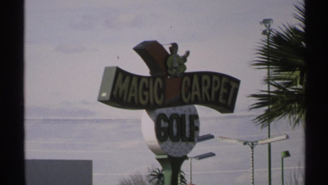 Magic Carpet Golf sign beside a roadside attraction with palm fronds and pale sky.