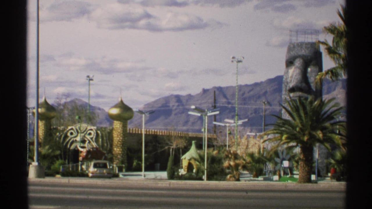 Golden domes, tiger-head sculpture, large stone face, palm tree, parked car, and mountain backdrop.