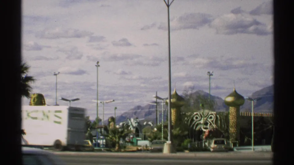 1972 Arizona roadside view with a passing white vehicle in front of domed structures, a tiger-head sculpture, cars, and mountains.