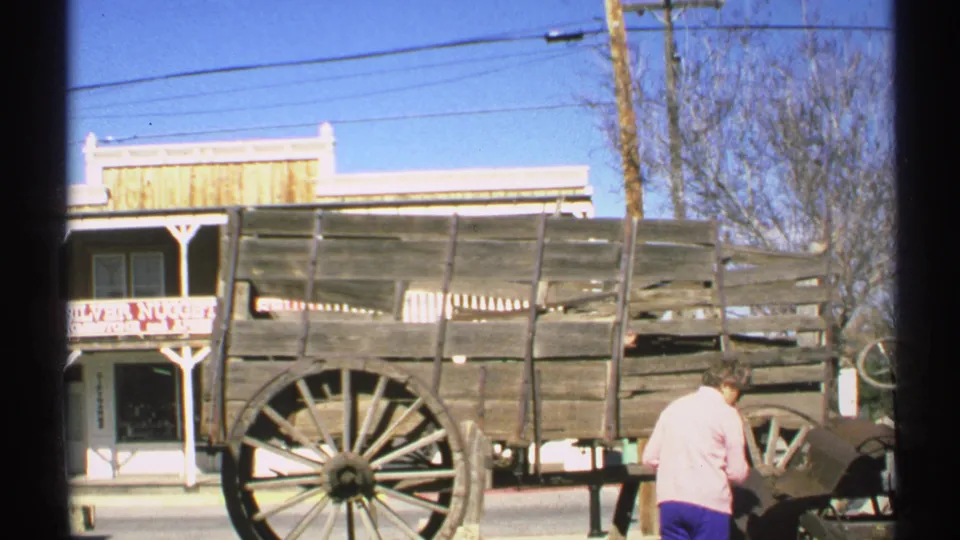 1972 Arizona frame showing a rustic wooden wagon beside a Silver Nugget storefront, with a person near the wagon and utility lines overhead.