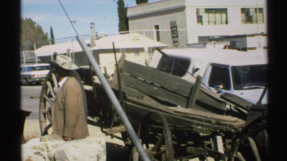 The 1972 Arizona frame shows a man in a cowboy hat near old wagon equipment, with 1970s cars and a roadside building in view.