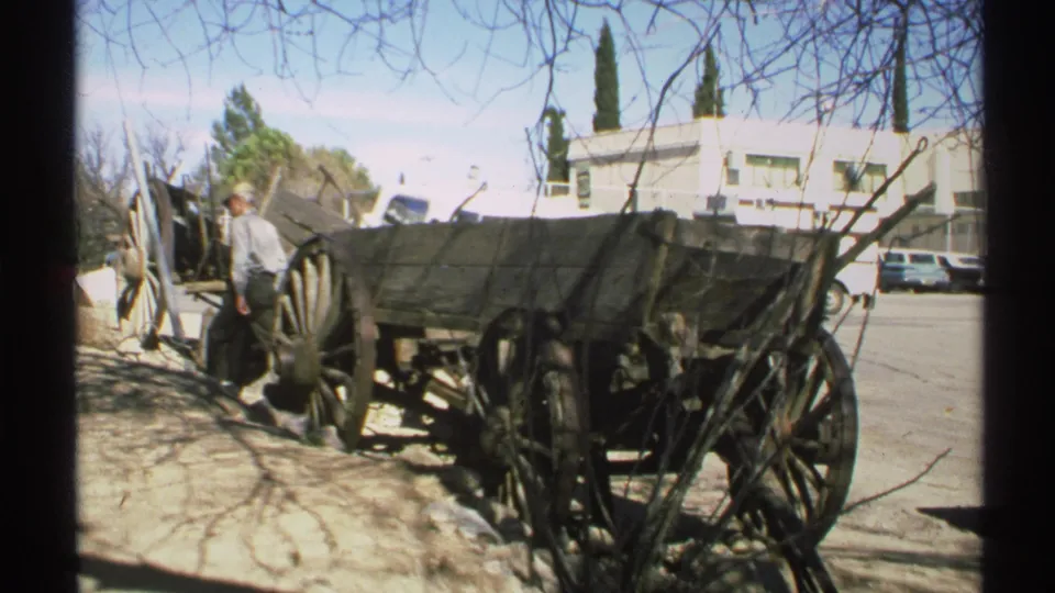 In the final 1972 Arizona frame, a man stands beside the old wooden wagon while cars, a roadside building, and bare branches remain visible.
