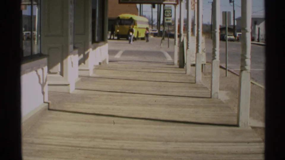 A 1972 Arizona street view from a covered porch shows a yellow school bus near the end of a wide wooden sidewalk.