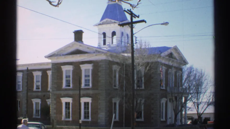 1972 Arizona 8mm frame showing a red brick building with white trim, a blue cupola, overhead wires, and a partial street view.