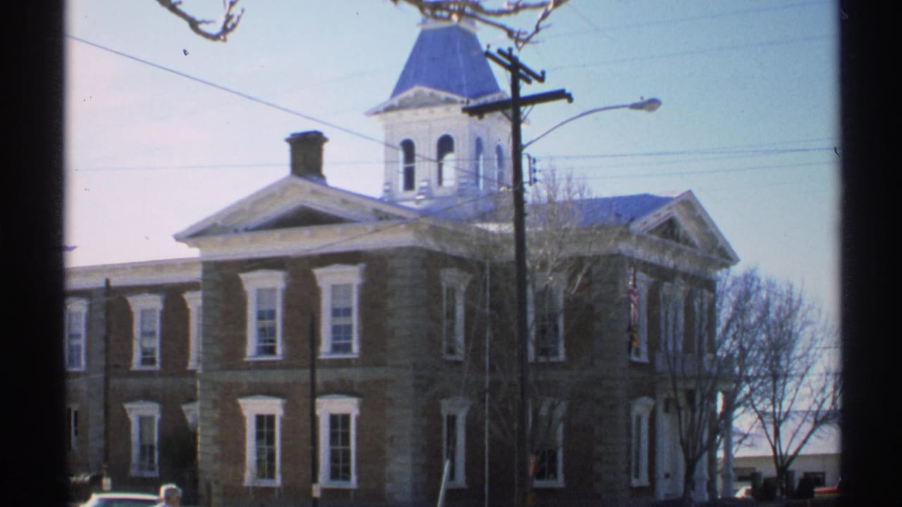 Brick building facade with cupola, white windows, bare tree branches, and overhead wires.