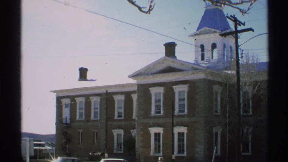 1972 Arizona frame of the building corner and cupola, with bare trees, utility lines, and a partial vehicle along the street.